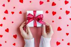 女手持有礼物白色包装纸粉红色的背景红色的心