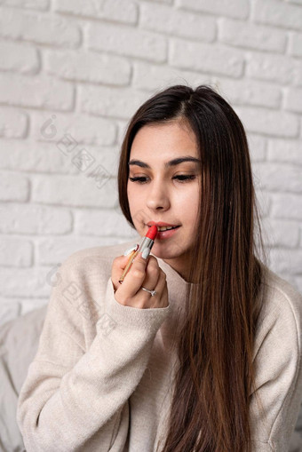 年轻的浅黑肤色的女人女人坐着床上使着色嘴唇