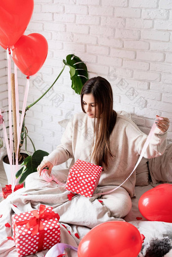 年轻的有趣的女人坐着床上庆祝<strong>情人节</strong>一天包装礼物