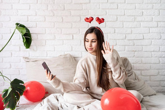 年轻的有趣的女人坐着床上庆祝情人节一天聊天移动电话