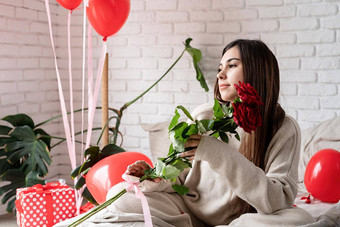 年轻的美丽的女人坐着床上庆祝<strong>情人节</strong>一天持有红色的玫瑰