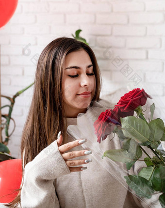 快乐笑美丽的女人坐着床上庆祝<strong>情人节</strong>一天持有红色的玫瑰