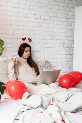 年轻的美丽的女人坐着床上庆祝情人节一天工作移动PC