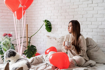 年轻的浅黑肤色的女人女人坐着床上庆祝情人节一天持有杯咖啡