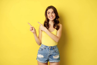 肖像时尚的夏天女孩浅黑肤色的女人女人显示指出手指左广告站黄色的背景