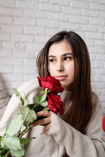 年轻的美丽的女人坐着床上庆祝情人节一天持有红色的玫瑰