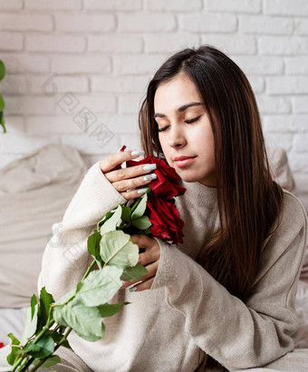 年轻的美丽的女人坐着床上庆祝<strong>情人节</strong>一天持有红色的玫瑰