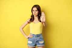时尚的女人显示停止拒绝禁止手势下降不赞成站黄色的背景