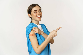 微笑护士女医疗保健工人实习医生风云指出手指显示补丁肩膀疫苗接种运动科维德流感大流行概念白色背景