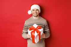 图像英俊的有胡子的男人。冬天毛衣圣诞老人他持有圣诞节礼物微笑现在包装丝带站红色的背景