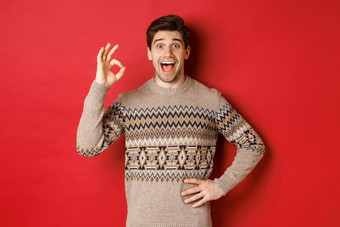 概念圣诞节庆祝活动冬天假期生活方式惊讶快乐男人。圣诞节毛衣显示标志神奇的红色的背景