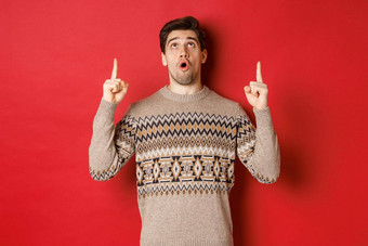 图像惊讶英俊的男人。圣诞节毛衣指出一年促销提供显示冬天假期广告红色的复制空间
