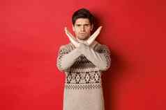 图像愤怒的英俊的男人。圣诞节毛衣告诉停止显示交叉手势限制禁止行动站红色的背景