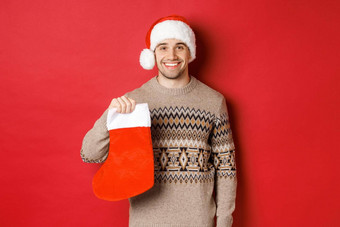 概念冬天假期一年庆祝活动图像英俊的微笑男人。圣诞老人他毛衣持有圣诞节长袜礼物糖果站红色的背景