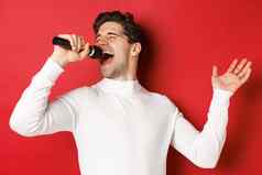英俊的的家伙白色毛衣唱歌首歌持有麦克风执行卡拉ok酒吧站红色的背景
