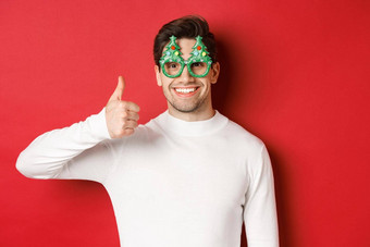 概念圣诞节冬天假期庆祝活动特写镜头英俊的微笑男人。穿聚会，派对眼镜白色毛衣显示竖起大拇指推荐一年促销