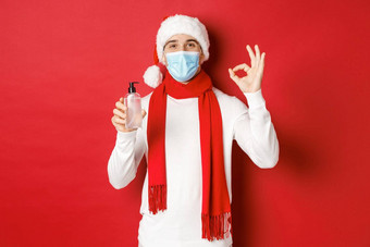 概念科维德圣诞节假期流感大流行有吸引力的男人。圣诞老人他医疗面具显示<strong>标志推荐</strong>手洗手液站红色的背景