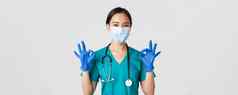 科维德冠状病毒疾病医疗保健工人概念自信微笑亚洲女医生护士医疗面具手套显示手势批准白色背景