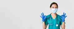 科维德冠状病毒疾病医疗保健工人概念自信微笑亚洲女医生护士医疗面具手套显示手势批准白色背景