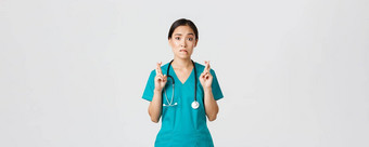 科维德医疗保健工人流感大流行概念充满希望的紧张亚洲女实习生实习医生风云等待新闻医生交叉手指咬唇相机祈祷