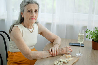 美丽的祖母灰色头发脸皱纹坐着表格首页窗口背景玻璃香槟母亲的一天快乐退休