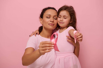 可爱的混血女人妈妈。拥抱女孩粉红色的服装显示粉红色的缎丝带相机象征乳房癌症一天10月月支持癌症病人幸存者
