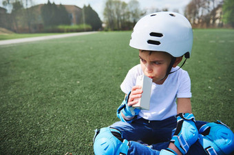 可爱的男孩滑板头盔保护设备休息坐着绿色草喝汁