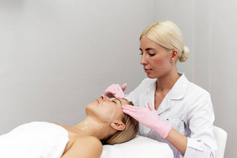 放松年轻的女人休息沙发上美容师按摩脸清理皮肤水疗中心治疗反老化