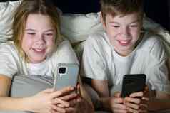 孩子们玩游戏智能手机平板电脑晚上毯子重写朋友社会网络社会媒体上瘾
