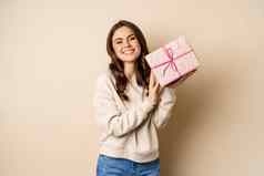 快乐美丽的女朋友持有粉红色的礼物盒子笑微笑快乐的概念假期庆祝活动米色背景