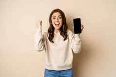 热情的女人欢呼显示手机屏幕智能手机应用程序接口站米色背景