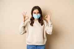 科维德流感大流行检疫概念年轻的女人穿医疗脸面具冠状病毒ο爆发显示标志站米色背景