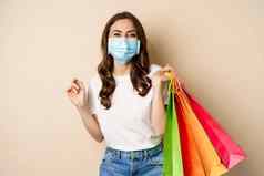 科维德流感大流行生活方式概念年轻的女人摆姿势医疗脸面具购物袋购物中心接种疫苗女孩商店个人保护设备米色背景