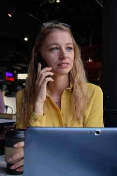 年轻的cauasian漂亮的女人咖啡商店移动PC调用智能手机