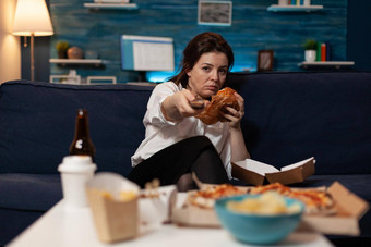 无聊女人坐着沙发吃美味的美味的汉堡持有远程切换<strong>渠道</strong>电视
