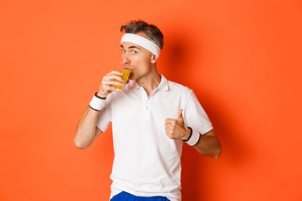 概念锻炼健身房生活方式肖像英俊的中年健身的家伙显示竖起大拇指喝汁站橙色背景