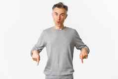 惊讶英俊的中年的家伙灰色毛衣问题产品指出手指惊讶站白色背景