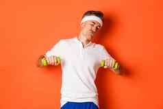 图像快乐中年的家伙体育锻炼哑铃站橙色背景
