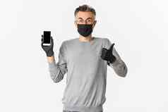 概念科维德社会距离生活方式图像满意英俊的中年男人。穿医疗面具手套眼镜显示竖起大拇指移动屏幕
