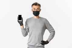概念科维德社会距离生活方式图像惊讶中年男人。发现在线显示智能手机屏幕惊讶穿医疗面具手套