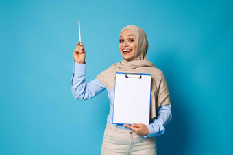 微笑阿拉伯女人持有剪贴板白色空白表纸点笔蓝色的背景空间文本