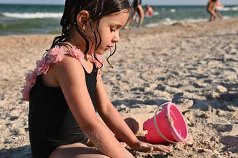 学龄前儿童女孩玩耙粉红色的玩具桶沙子建筑桑迪形状城堡享受日光浴夏天假期快乐童年健康娱乐概念