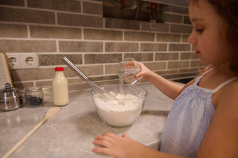 焦点手可爱的孩子女孩持有玻璃水倒碗面粉准备液体面团忏悔煎饼首页厨房