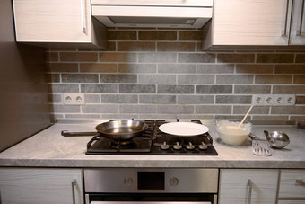 木勺子玻璃碗煎饼面糊不锈钢钢厨房餐具厨房工作台面白色板煎锅黑色的炉子前面视图