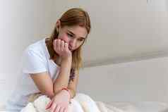 年轻的女人坐在床上持有头手伤心抑郁症首页头疼