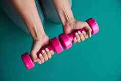 女人手持有粉红色的哑铃绿色体育运动席背景首页锻炼流感大流行锻炼健身房健身概念