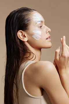 浅黑肤色的女人脸面具奶油清洁皮肤面部擦洗米色背景