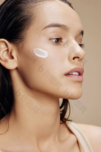 浅黑肤色的女人应用舒缓的脸面具化妆品米色背景