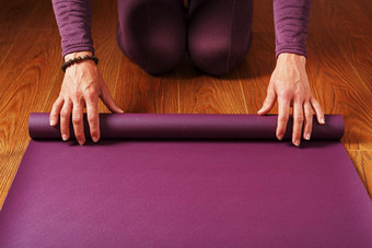 女孩折叠淡<strong>紫色瑜伽</strong>席实践锻炼木地板上