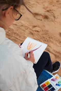 年轻的女人艺术家绘画旅行草图水彩海边